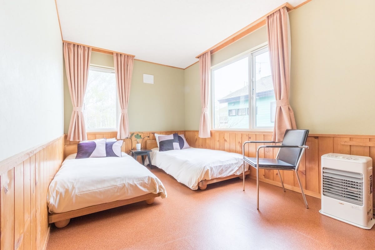 A room with two beds, a chair, a small table, and a heater.