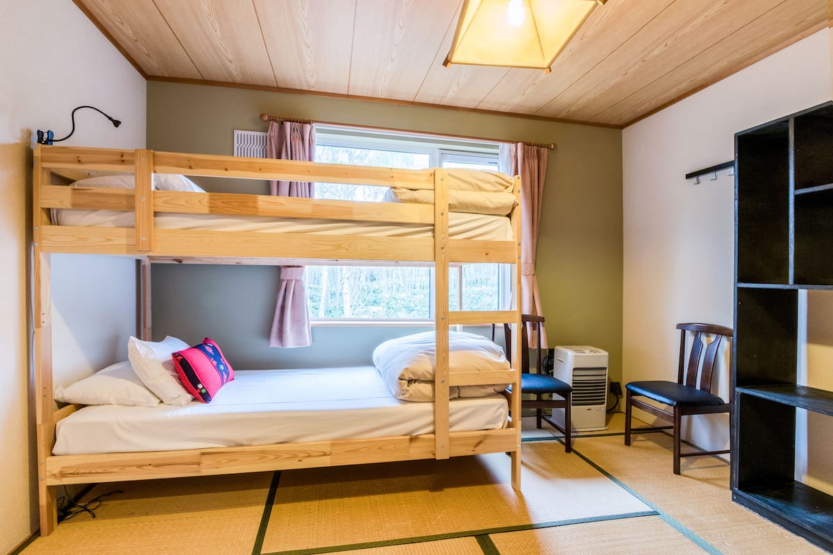 A bunk bed room with a window, a chair, and a heater.