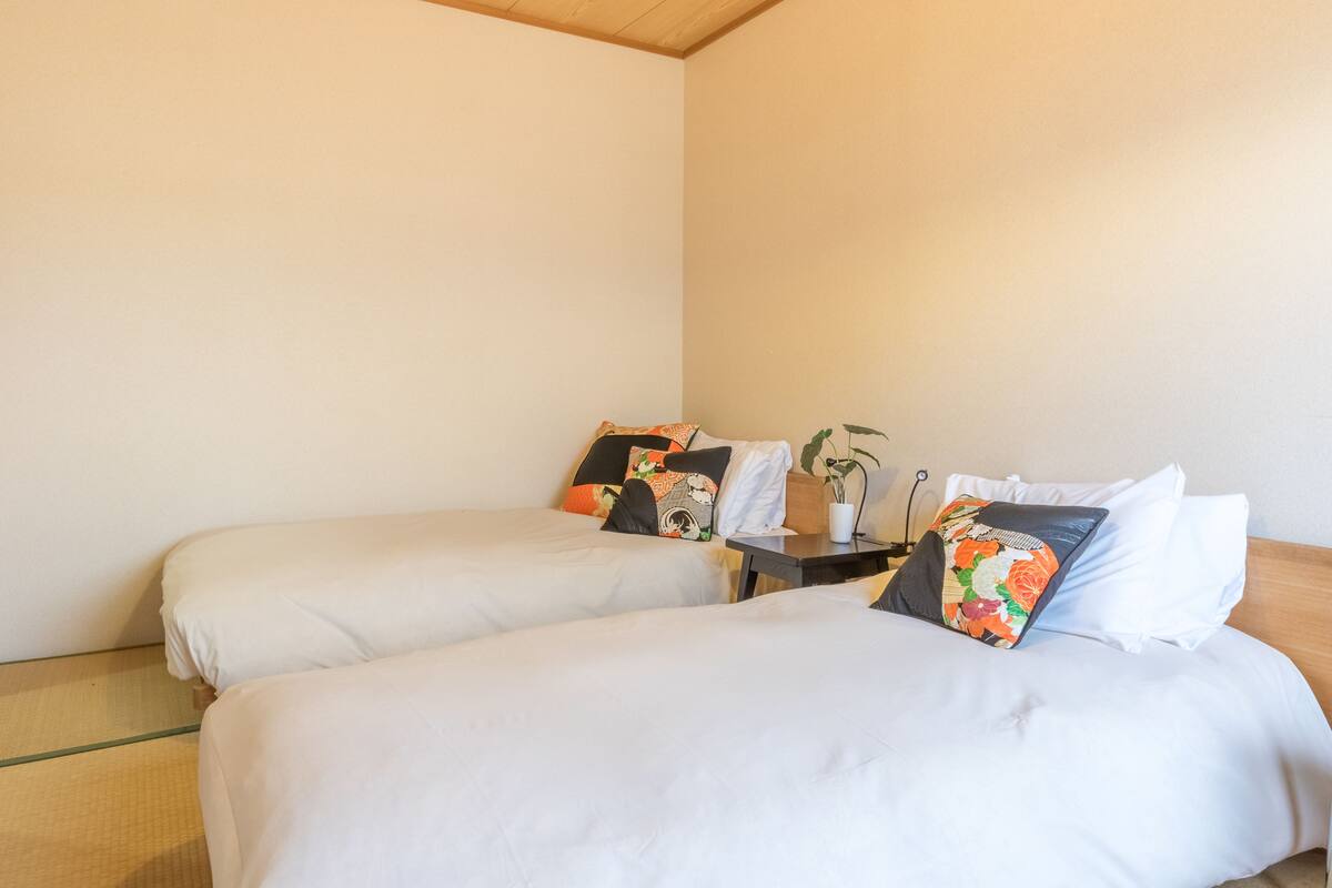 A hotel room with two single beds, a small table with a plant, and a wooden headboard.