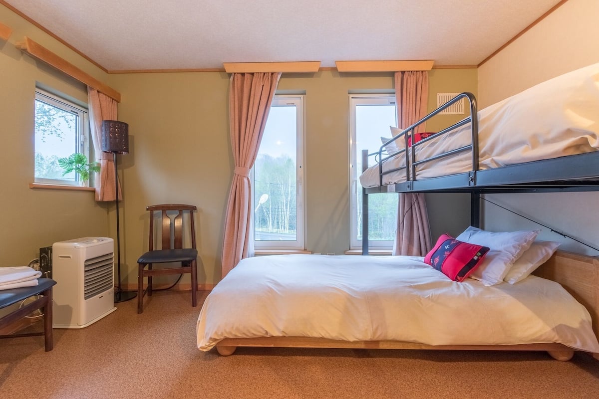 A hotel room with a bunk bed, a desk with a chair, a standing lamp, and a window with curtains.