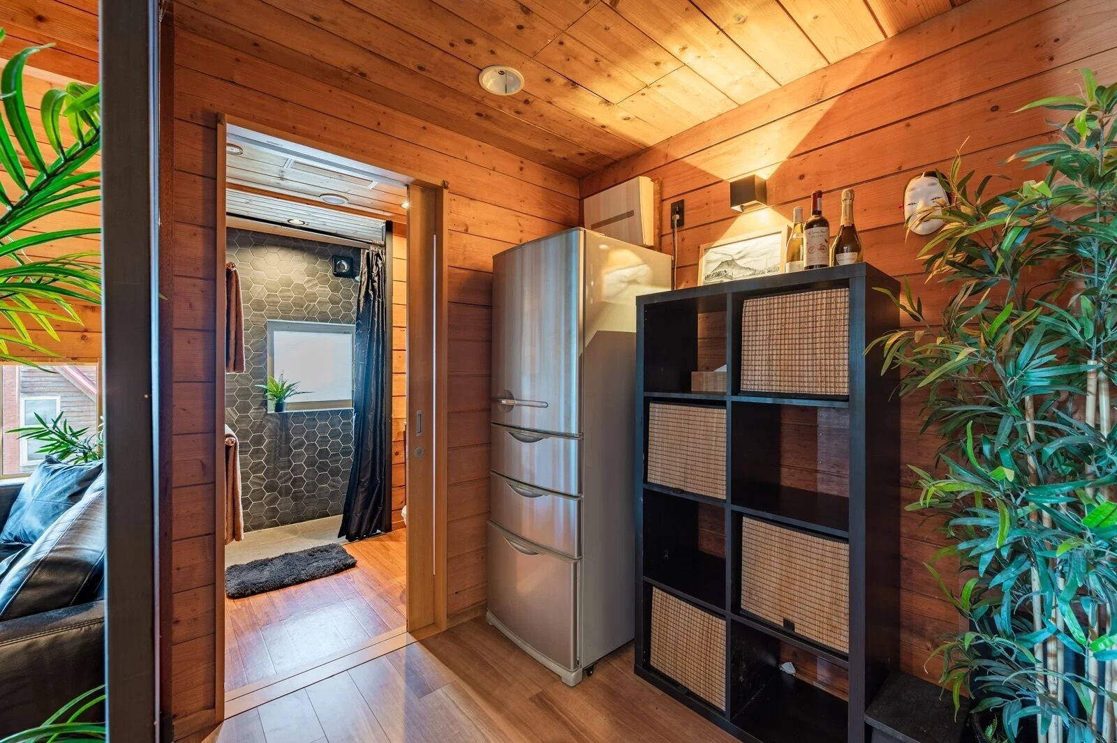 A wooden interior with a refrigerator, shelves, and a door leading to another room.