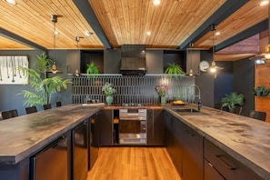 Une cuisine moderne avec des poutres apparentes en bois au plafond, un îlot central et des appareils électroménagers intégrés.