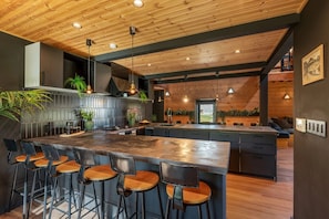 A modern kitchen with a large island, bar stools, and wooden ceiling. - Hooting Owl Lodge (Niseko)
