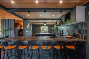 A modern kitchen with a central island, bar stools, pendant lighting, and a view of the outdoors. - Hooting Owl Lodge (Niseko)