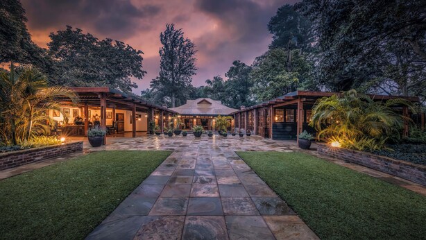 A spacious courtyard with a central open area, surrounded by lush greenery and a stone pathway. - Elewana Arusha Coffee Lodge (Arusha)