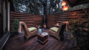 A wooden deck with wicker chairs and a table, surrounded by wooden railings and potted plants. - Elewana Arusha Coffee Lodge (Arusha)