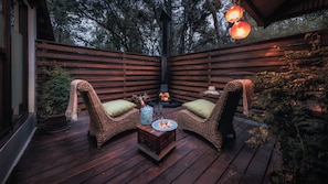 A wooden deck with wicker chairs and a table, surrounded by wooden railings and potted plants. - Elewana Arusha Coffee Lodge (Arusha)