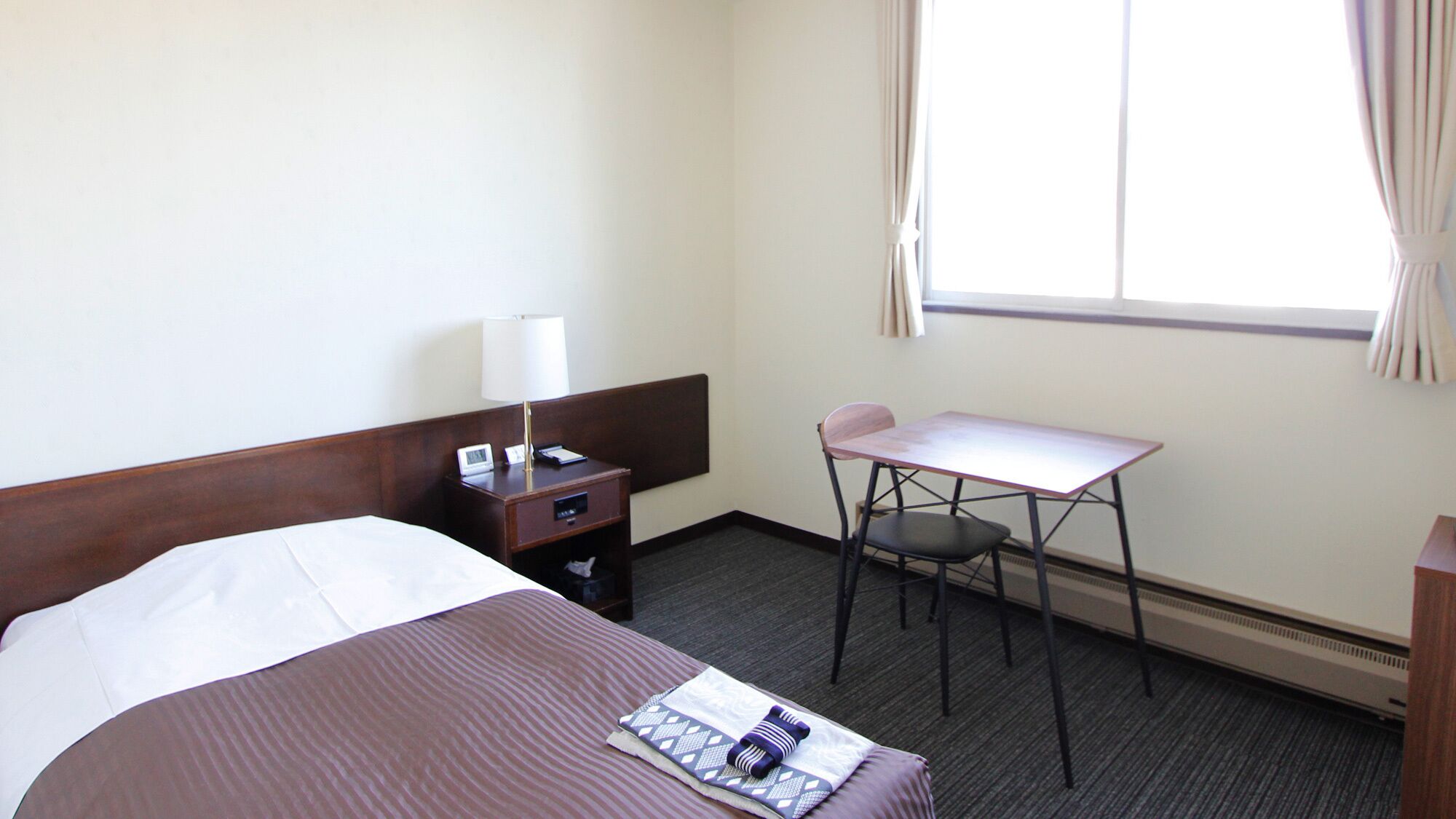 Ein Hotelzimmer mit Bett, Schreibtisch, Stuhl, Lampe und Fenster.