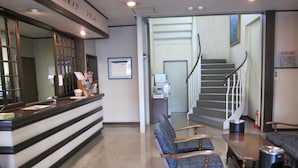A reception area with a counter, two armchairs, a trash can, and a staircase leading to another floor. - Hotel Sun Abashiri (Abashiri)