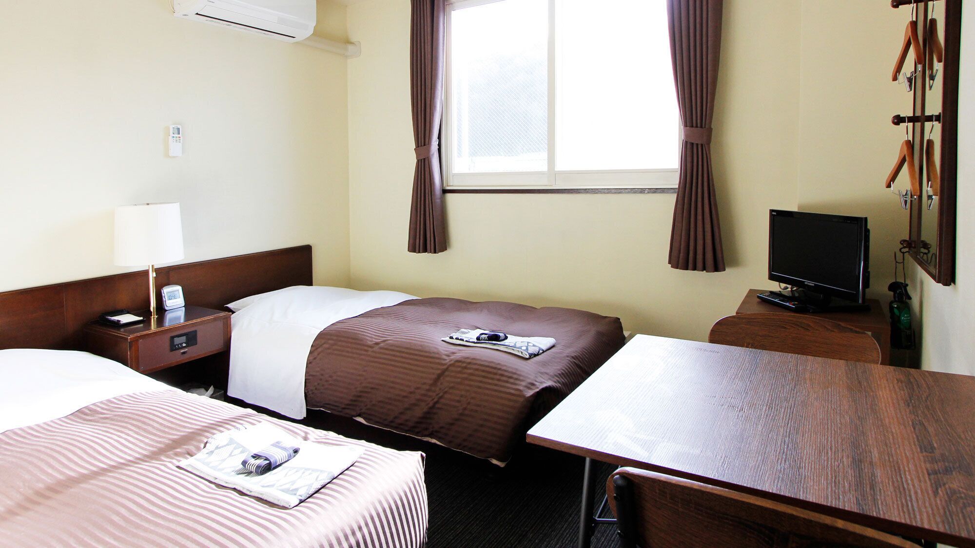 A hotel room with two beds, a desk, a television, and a window with curtains.