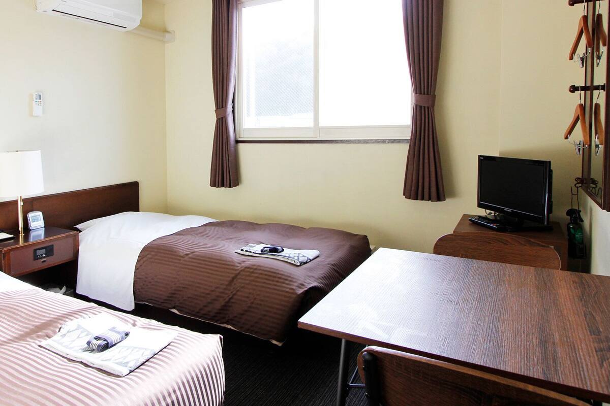 A hotel room with two beds, a desk, a television, and a window with curtains.