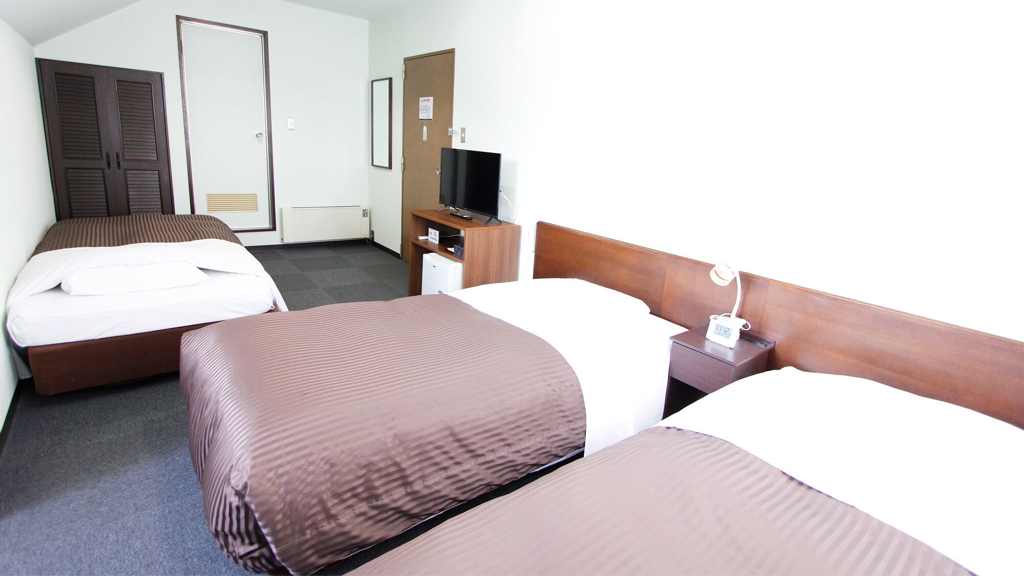 Ein Hotelzimmer mit zwei Betten, einem Fernseher, einem Schreibtisch und einem kleinen Kühlschrank.
