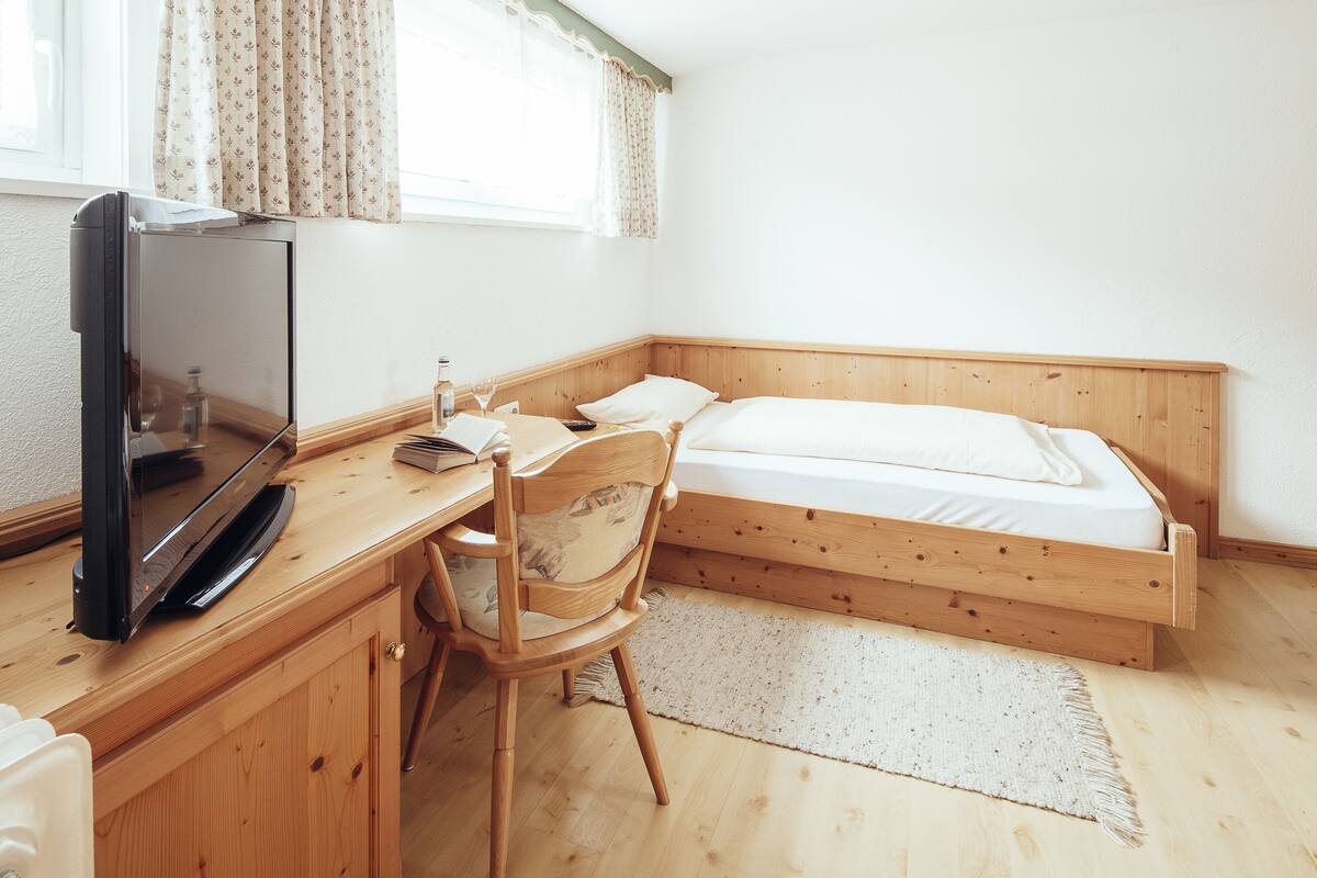A bedroom with a wooden bed, a desk with a television, and a chair.