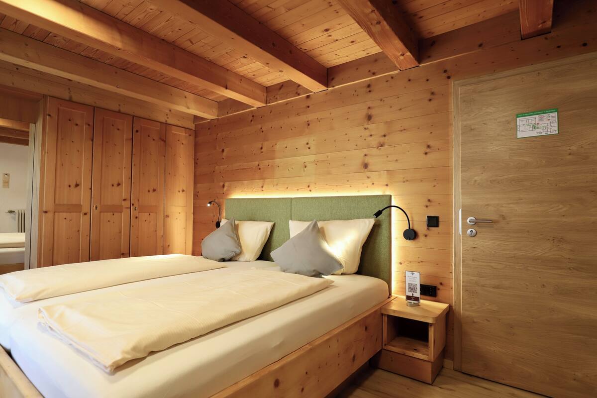 A wooden cabin-style bedroom with a double bed, a nightstand, and a door.
