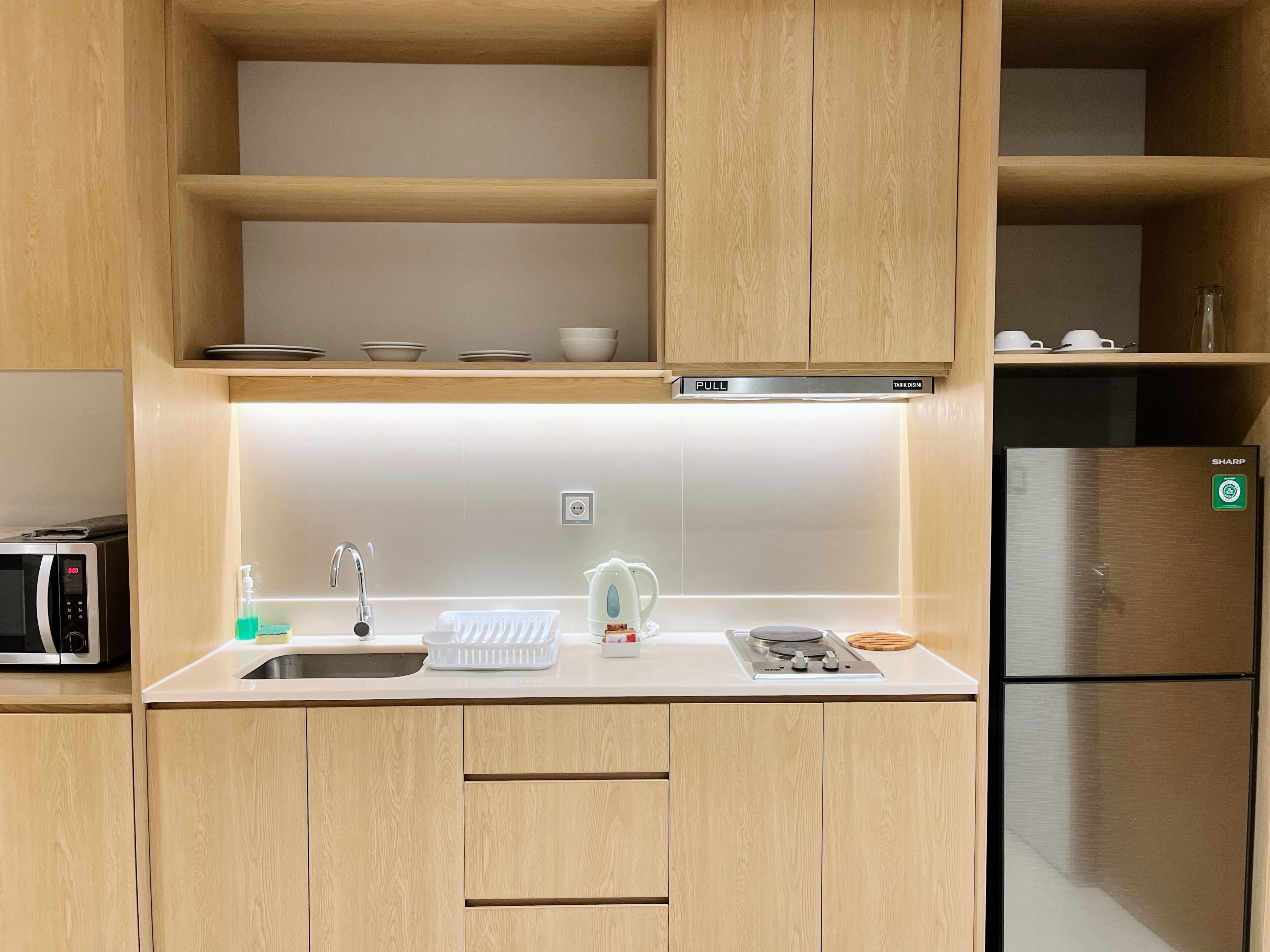 Een moderne keuken met houten kastjes, een roestvrijstalen koelkast, een magnetron, een spoelbak en een waterkoker.