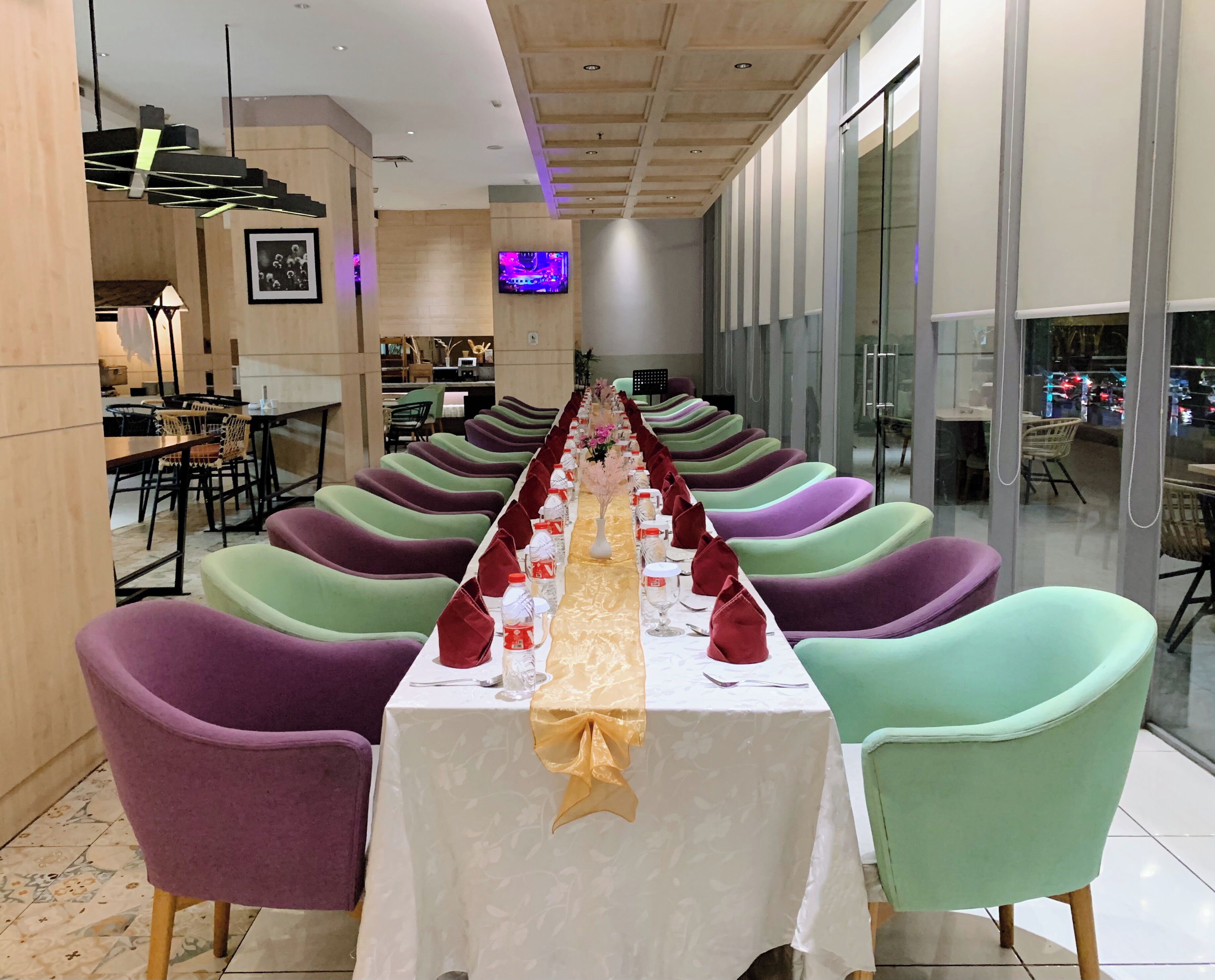 A long dining table with colorful chairs, a television screen, and a decorative centerpiece.