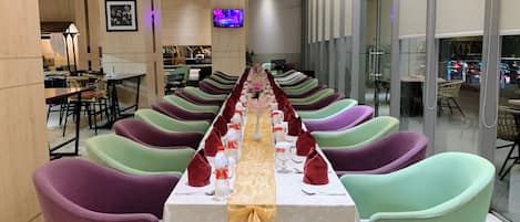 A long dining table with colorful chairs, a television screen, and a decorative centerpiece.