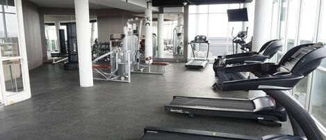 Un gimnasio con cintas de correr, máquinas de pesas y un ventanal grande.