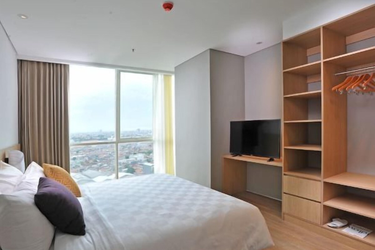 Un dormitorio moderno con una cama grande, televisión, armario y vista a la ciudad.
