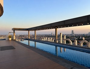 Una piscina en la azotea con vistas a la ciudad, una zona de estar cubierta y una planta en maceta.