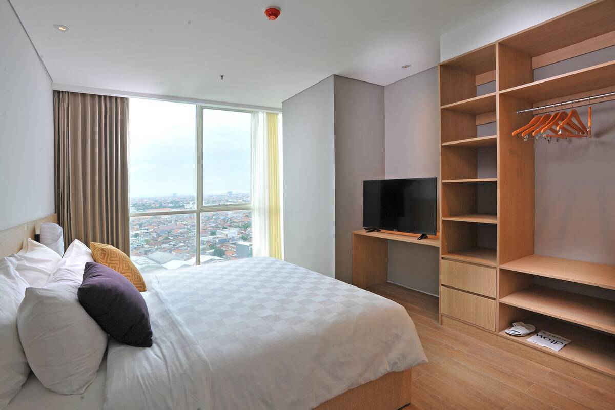 A hotel room with a large bed, a TV, a wardrobe, and a view of the city.