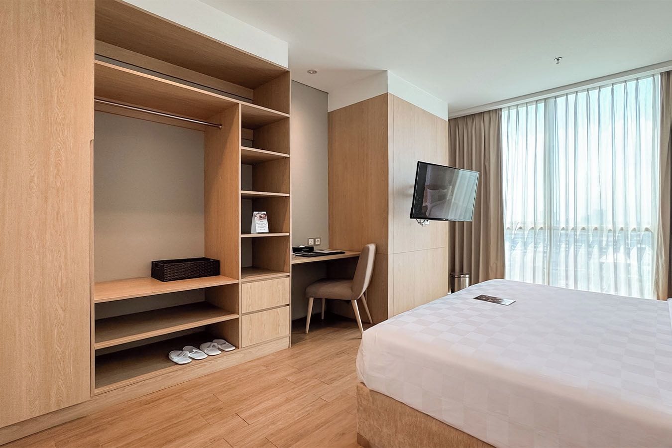 Una habitación de hotel con un armario grande, un escritorio con una silla, una cama y un televisor montado en la pared.