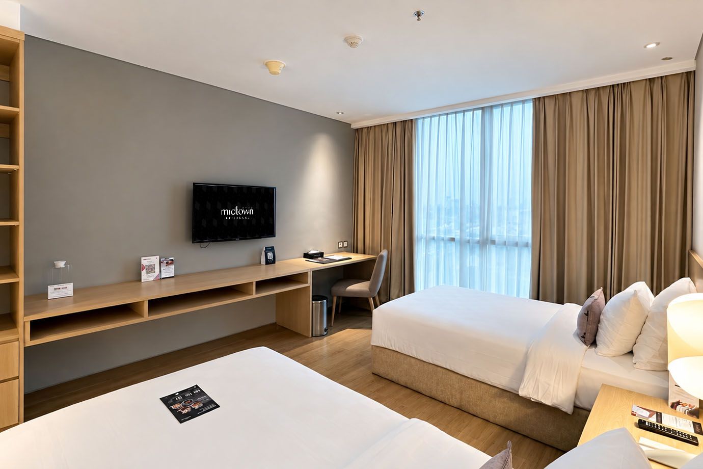 A hotel room with a bed, a desk, a television, and a large window with curtains.