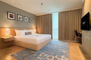 Habitación de hotel con una cama grande, mesitas de noche, un televisor de pantalla plana y vistas a la ciudad a través de la ventana.