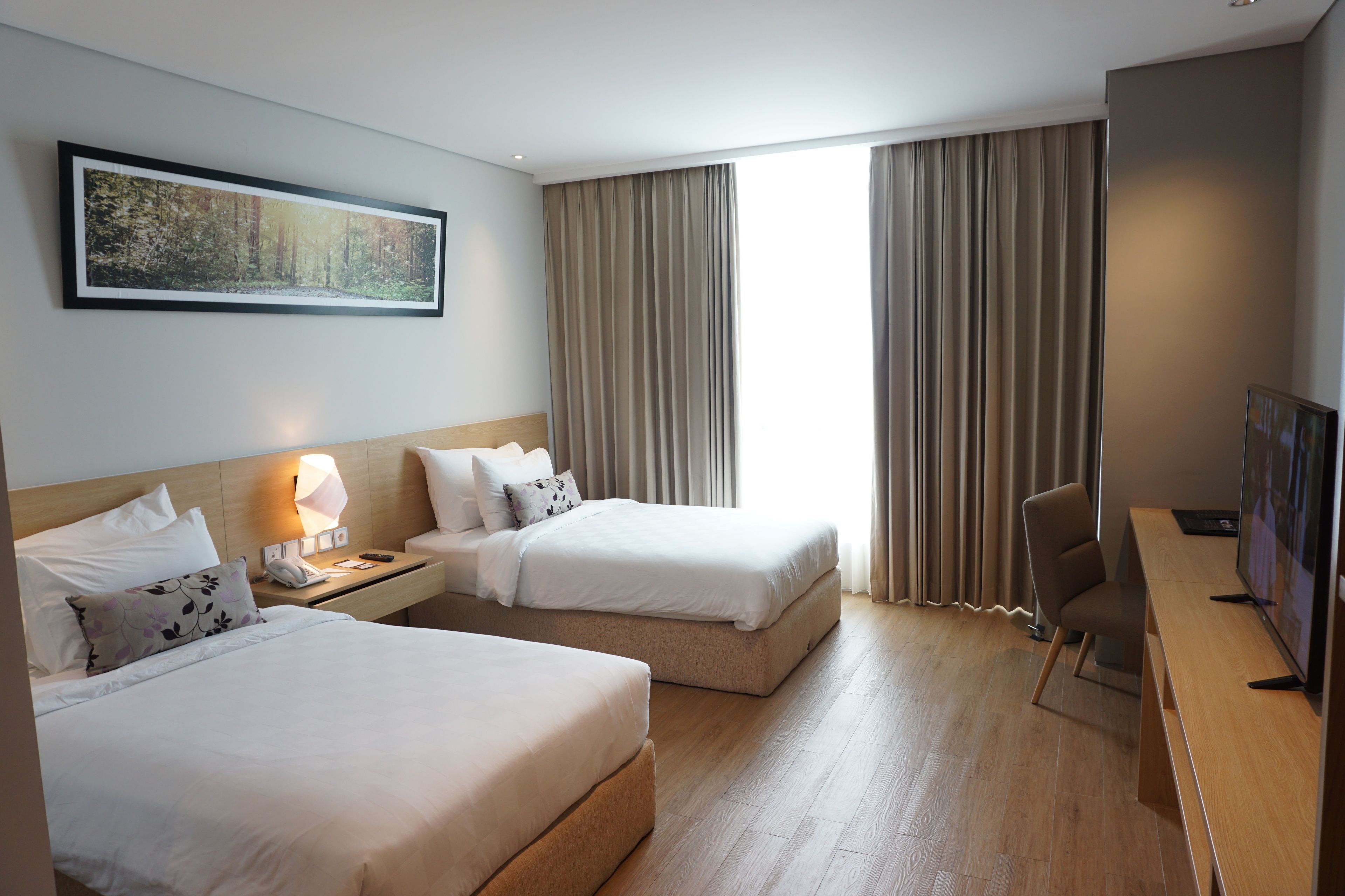 Een hotelkamer met twee bedden, een bureau, een stoel, een televisie en een groot raam met gordijnen.