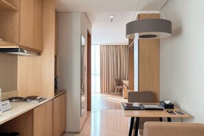 A modern kitchen with wooden cabinets, a built-in stove, and a dining area with a table and chairs. - Midtown Residence Surabaya (Surabaya)