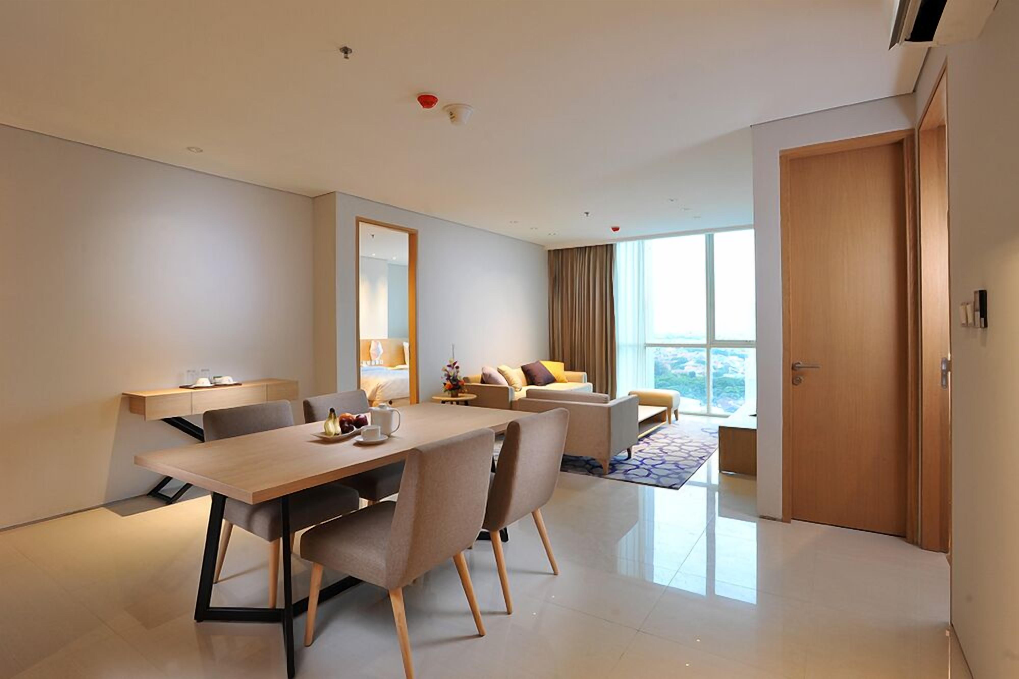 A modern hotel room with a dining area, a sofa set, a large window, and a door.