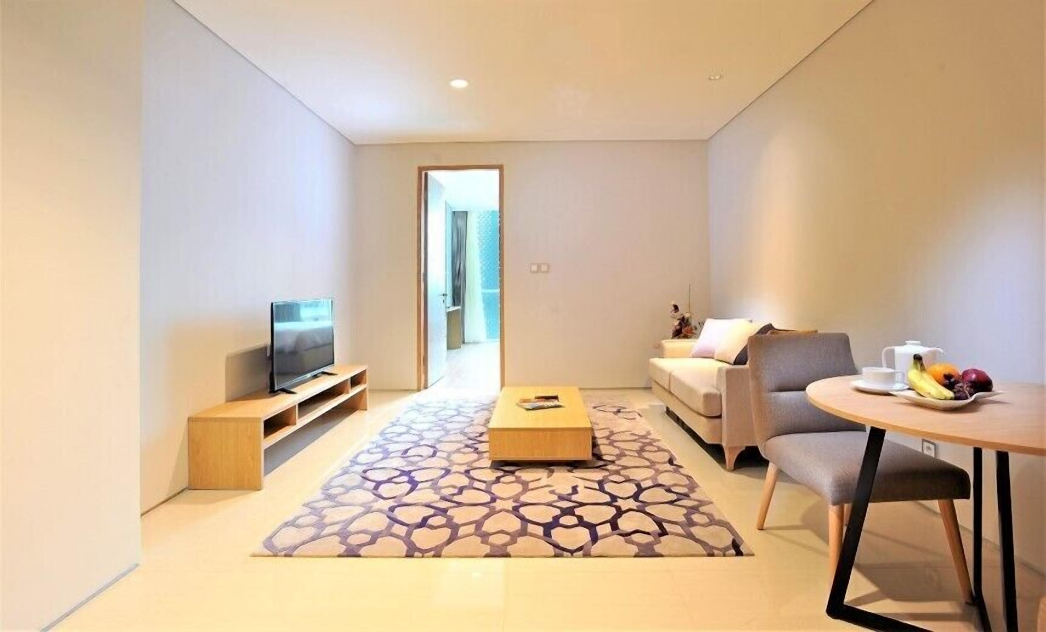 A modern living room with a flat-screen TV, a sofa, a coffee table, and a dining area with fruit.