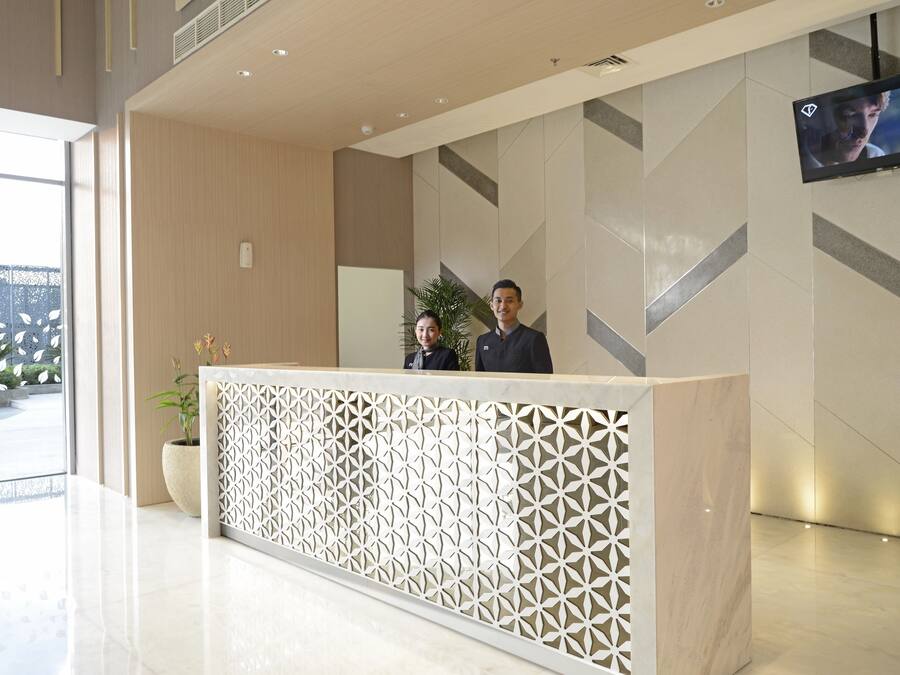 Een receptiebalie met een geometrisch patroon, een aan de muur bevestigde televisie en een kamerplant.