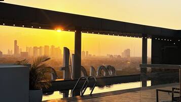 A rooftop terrace with a city skyline view at sunset, a pool, and lounge chairs.
