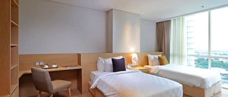 A hotel room with two beds, a desk, a chair, and a large window with a city view.