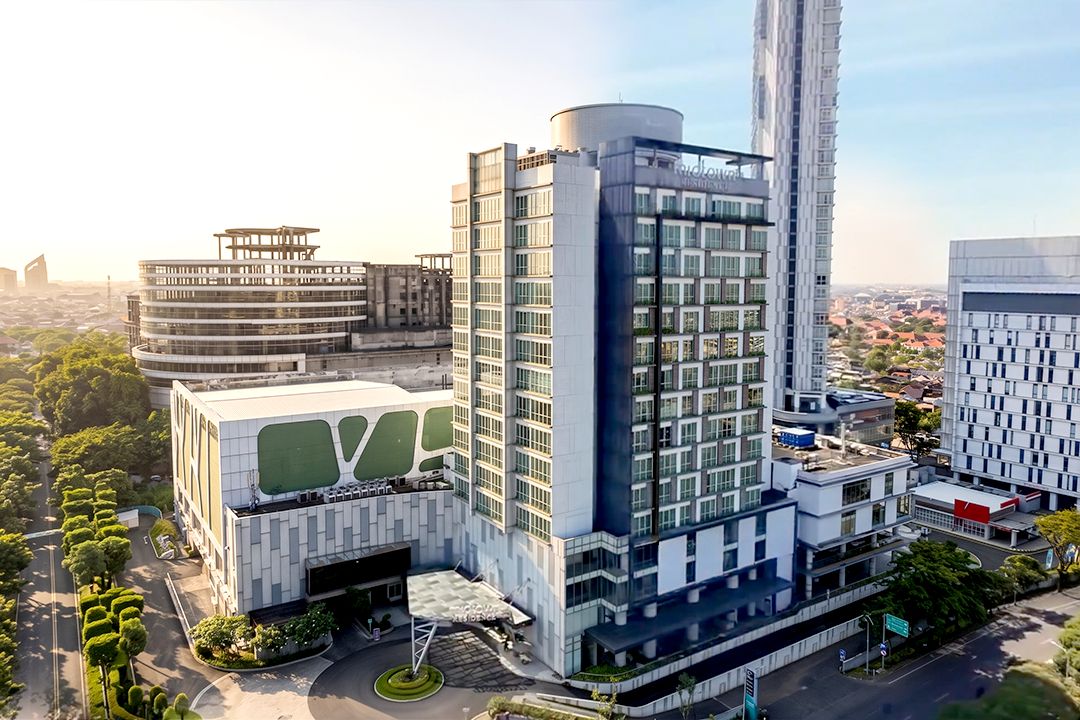 A modern hotel with a prominent cylindrical tower, a circular building with a green roof, and a rectangular building with a large glass facade.