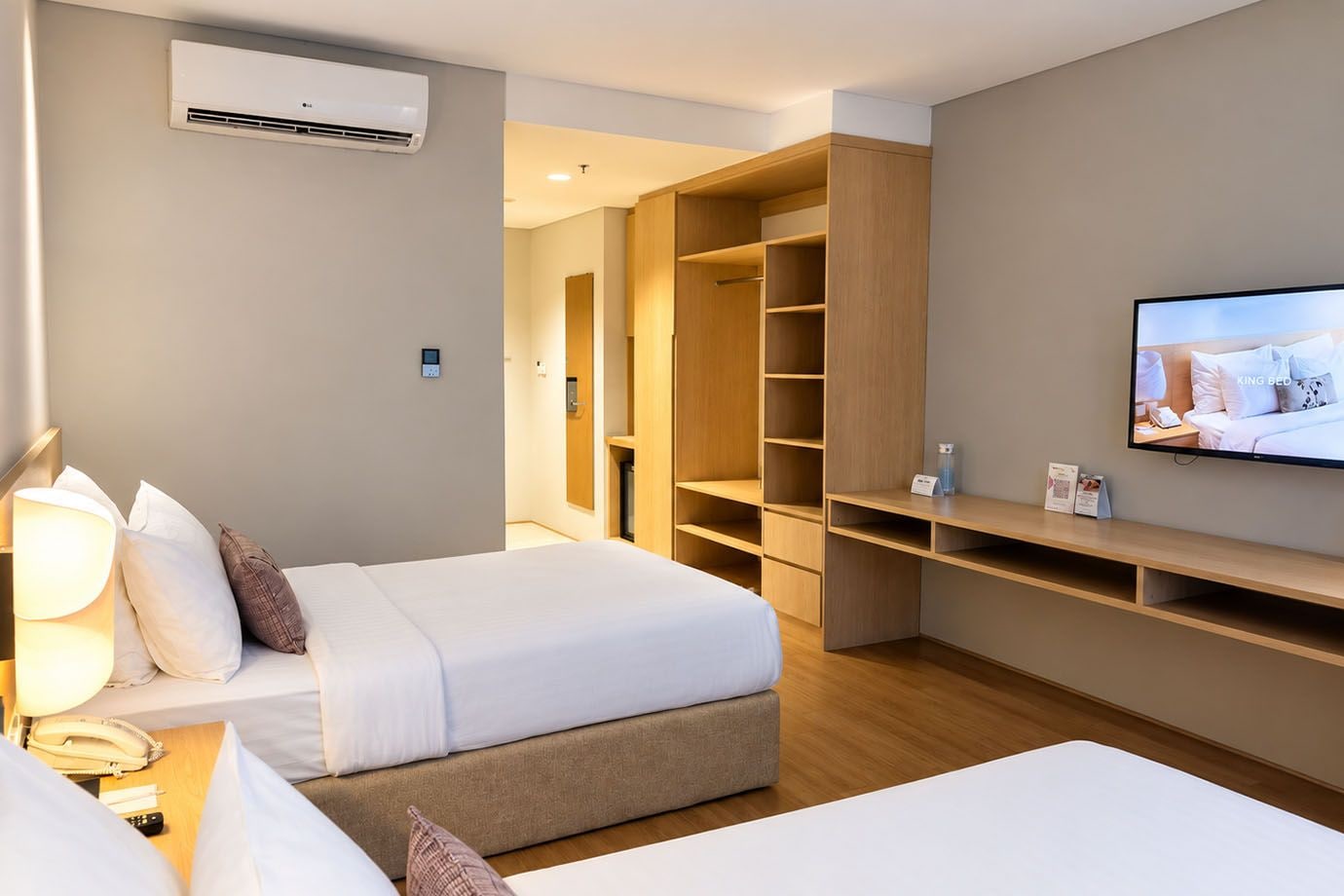 A hotel room with two beds, a TV, a bedside lamp, a phone, and a large wardrobe.
