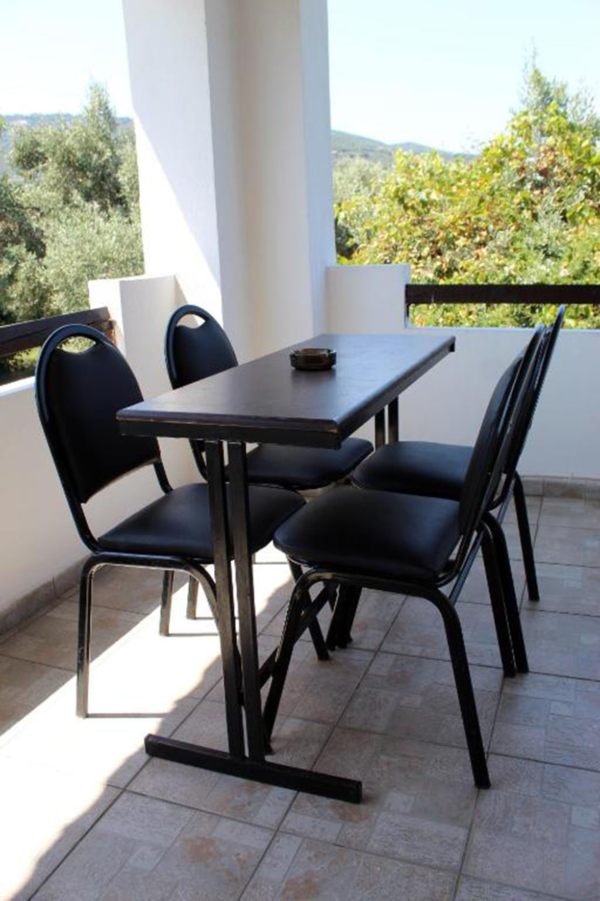 Uma varanda com mesa e cadeiras, oferecendo uma vista panorâmica com árvores e colinas.