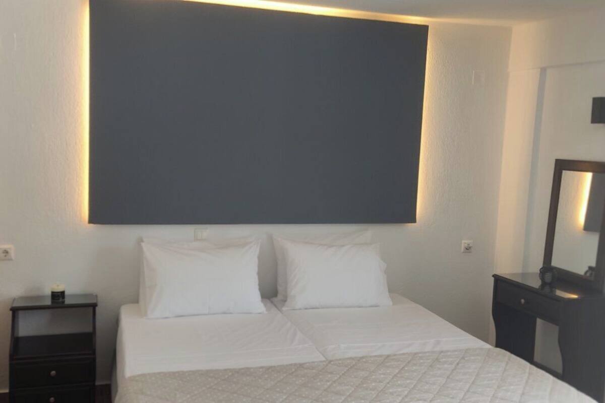 A hotel room with a large bed, a bedside table, a nightstand, a dresser, and a mirror.