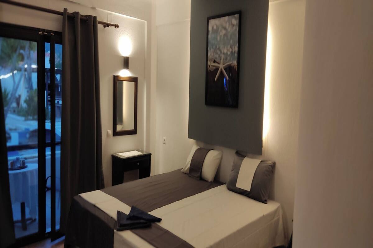 A hotel room with a bed, a nightstand, a wall-mounted mirror, and a painting.