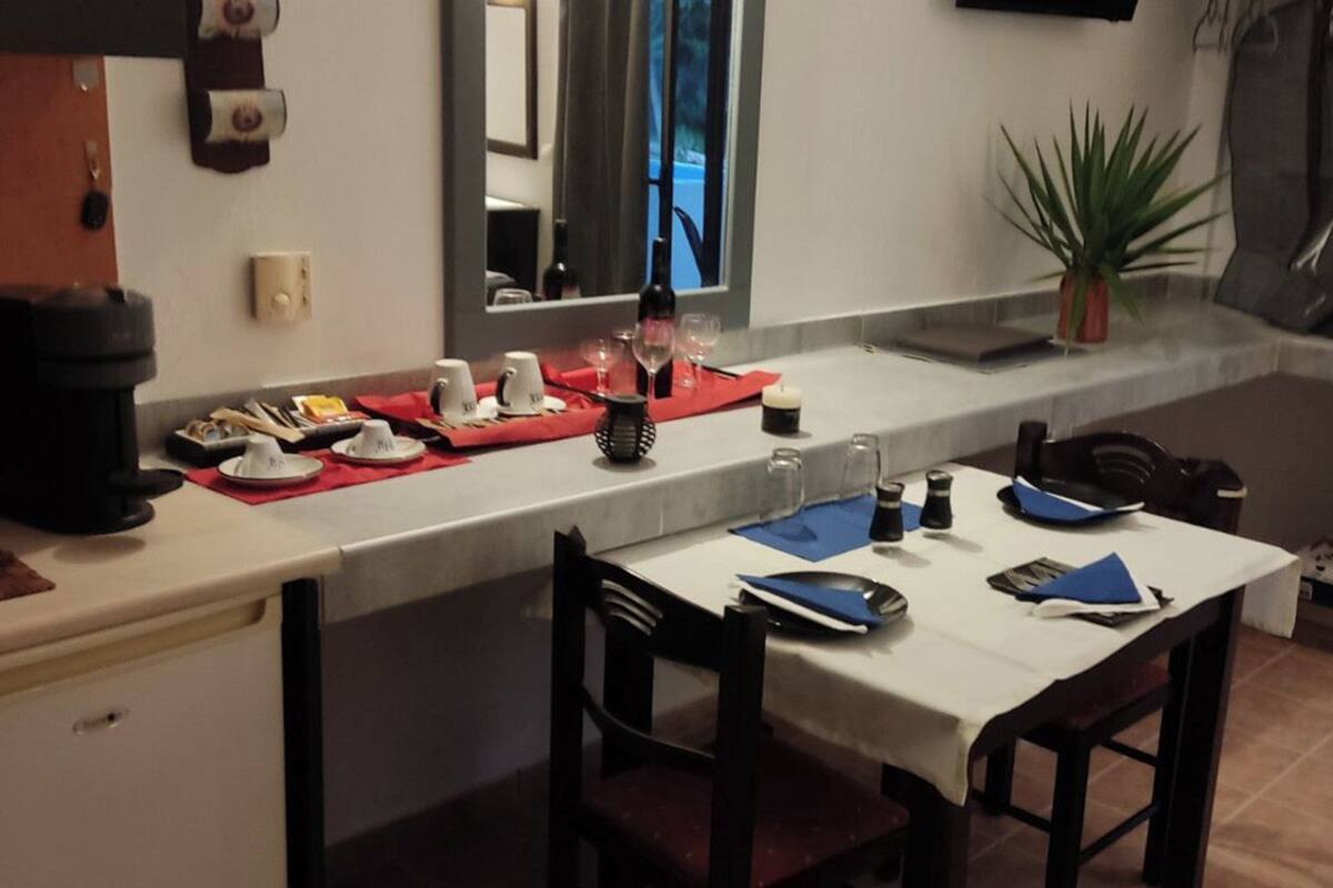 A kitchen with a dining table set for two, a coffee machine, and a potted plant.