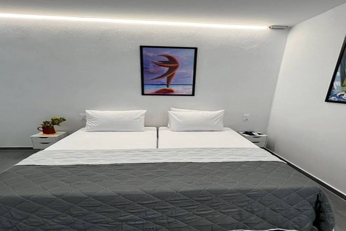 A double bed with a grey quilt, white pillows, and a framed artwork on the wall.