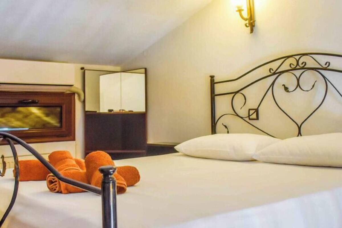 A neatly made bed with white linens, a metal headboard, and orange towels.