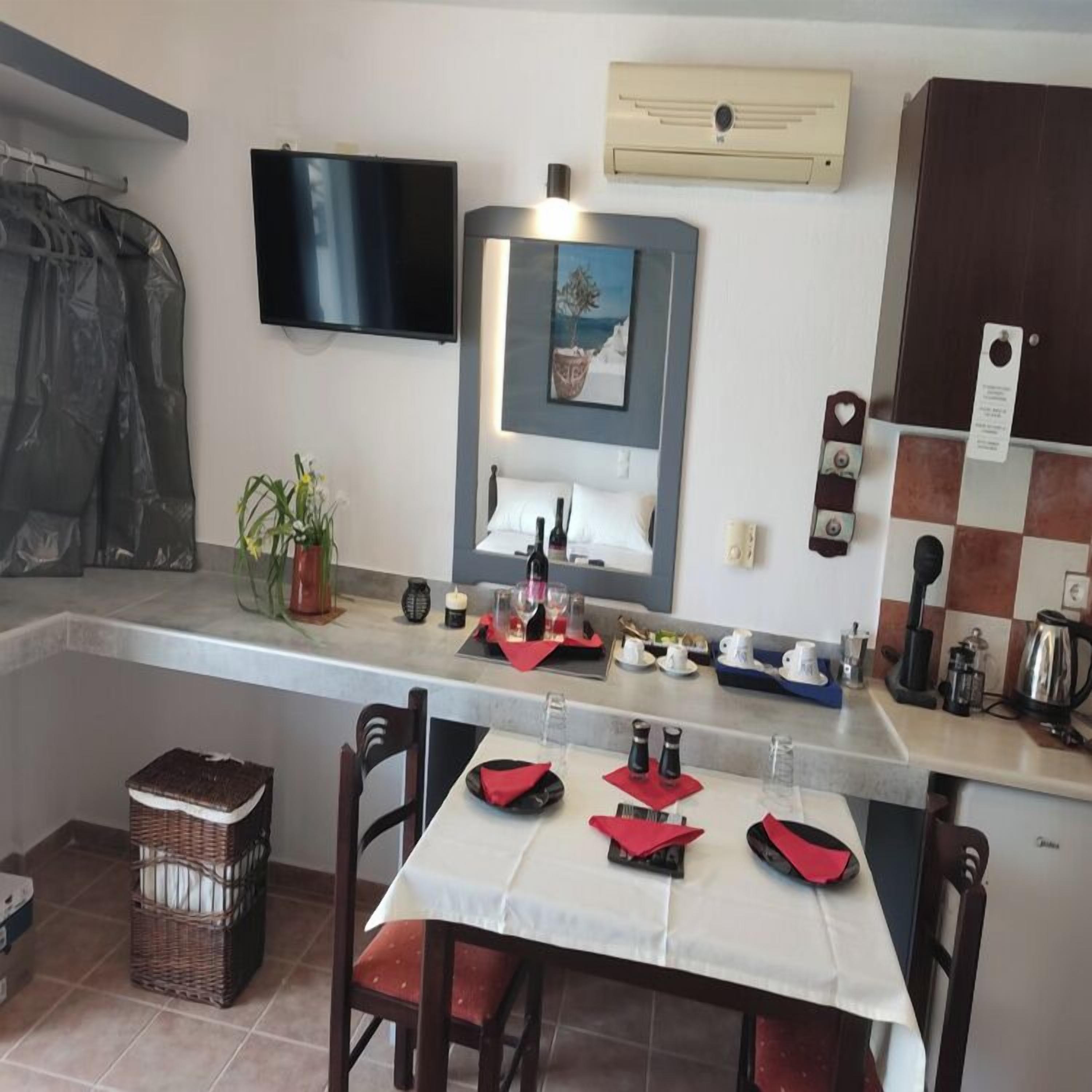 A compact kitchen with a dining area, a flat-screen TV mounted above the counter, a small potted plant, and a coffee machine.