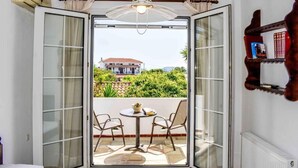 A room with a bed, a table with chairs, and a view of a house through open sliding doors. - Skiathos Holiday Resort (Skiathos)