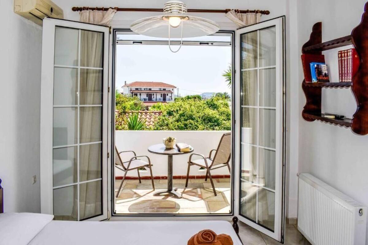 A room with a bed, a table with chairs, and a view of a house through open sliding doors.
