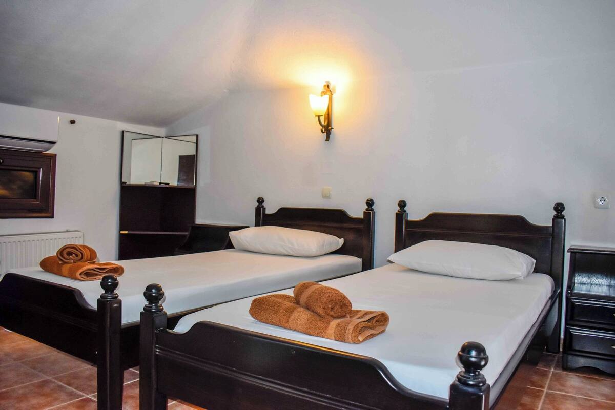 A hotel room with two single beds, a nightstand, a lamp, and a mirror.