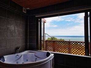 A bathroom with a large bathtub, a view of the ocean, and a balcony with a lattice fence. - Nagahama Beach Resort Kanon (Nakijin)