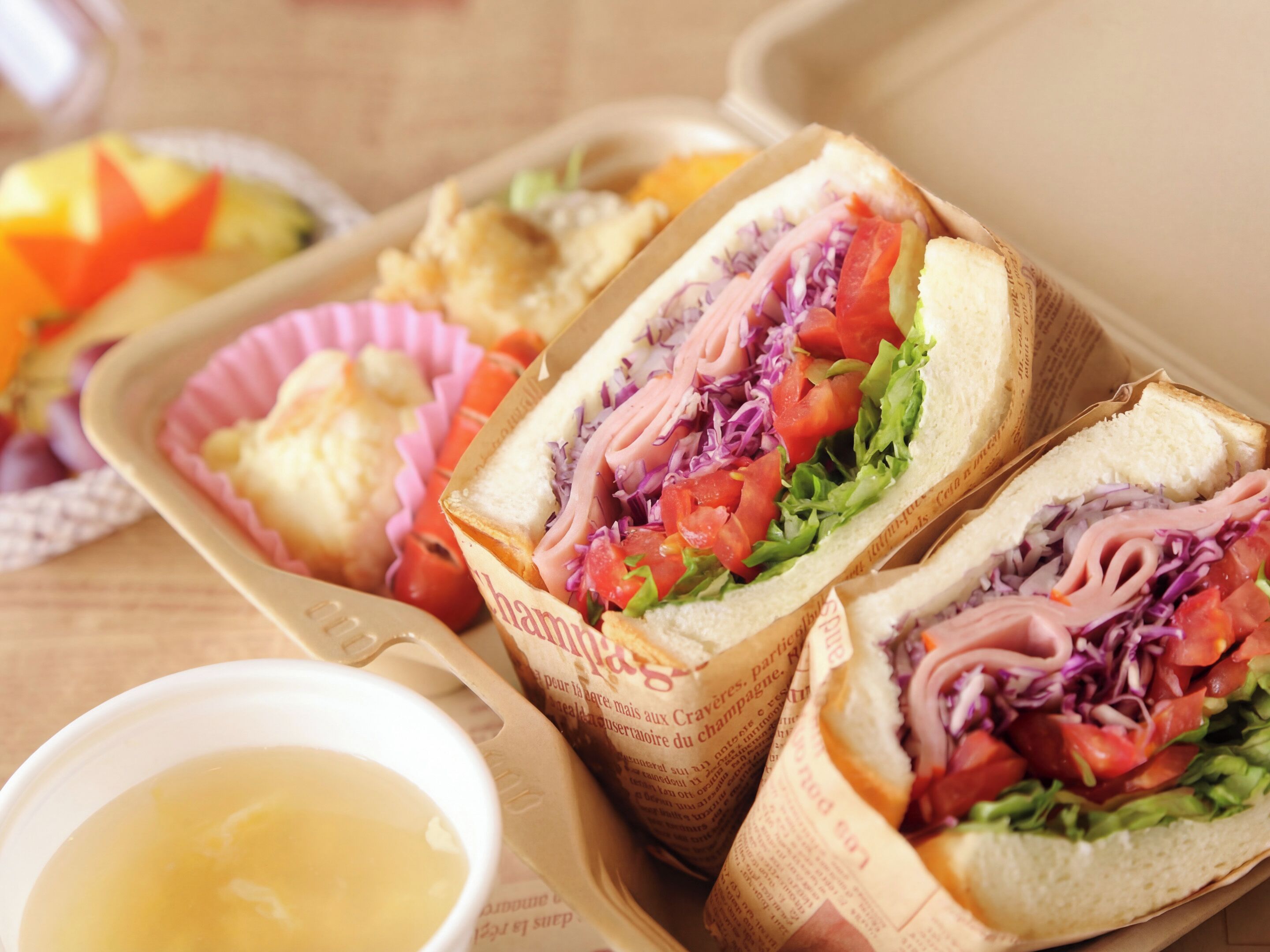 A sandwich with lettuce, tomatoes, and red onions in a paper container.