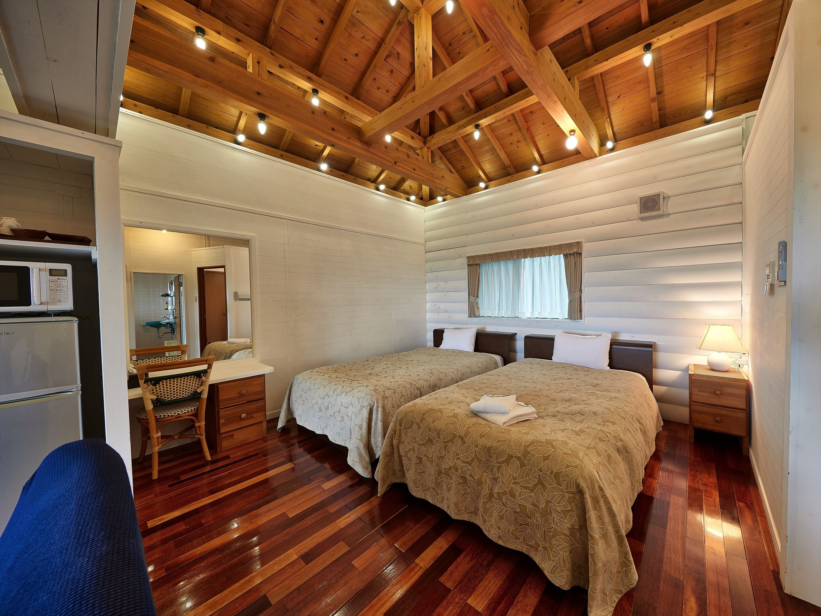 Una habitación acogedora de estilo cabaña con dos camas, techo de madera, kitchenette pequeña y una ventana con cortinas.